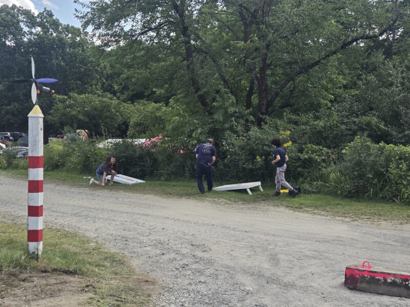 A group of Stellafane attendees play a round of cornhole on a solar system themed set against a background of leafy green trees and bushes. 