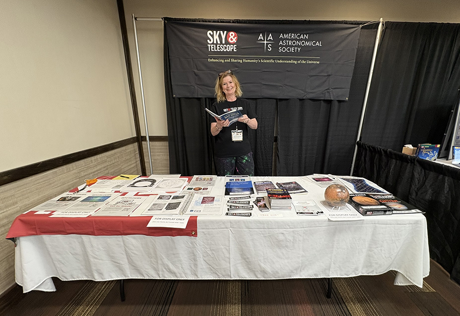 Diana Hannikainen tending to the booth at ASTROCON2025, where a table is laden with S&T products, books, and issues