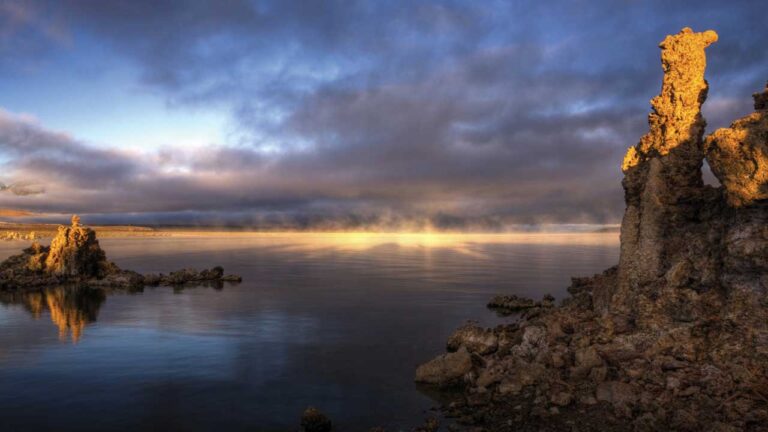 a large body of water with a rock formation in the front and a cloudy sky