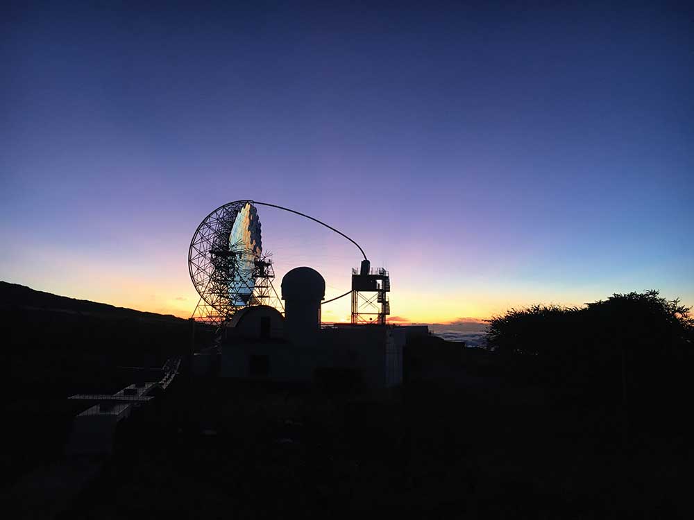 a sunset with a large telescope and satelittle dish in silhouette