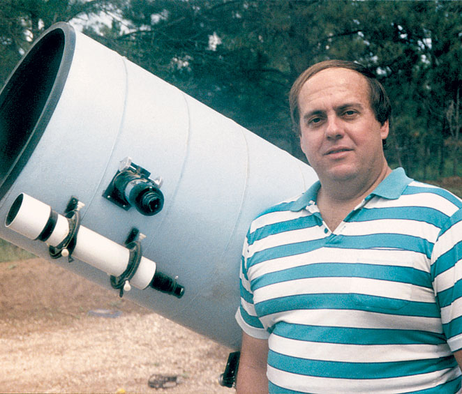Photo of Alan Hale in a blue and white striped shirt with brown hair in front of a large white telescope