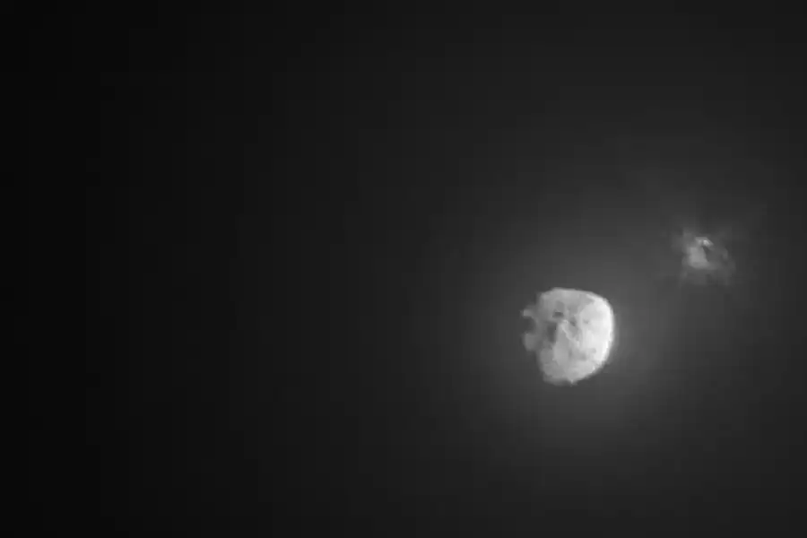view of Didymos-Dimorphos system minutes after hit shows larger intact asteroid and debris coming from smaller asteroid that was hit