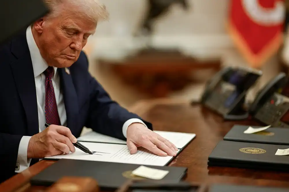 President Trump signing document on wooden desk