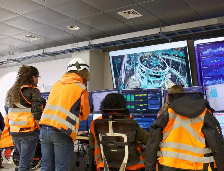 Orange-vested engineers investigate data reported on various screens large and small