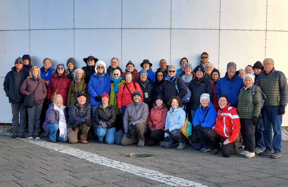 two rows of people standing in front of a white wall outside