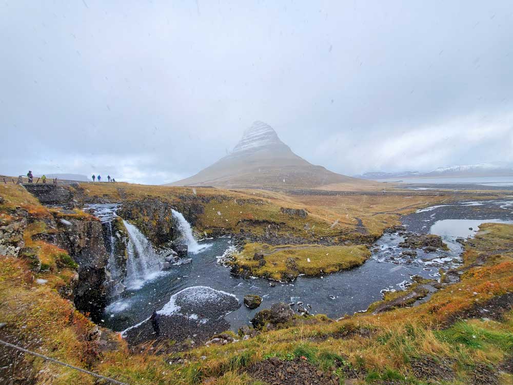 a mountain in the distance with haze around with and a waterfall with a river in the foreground