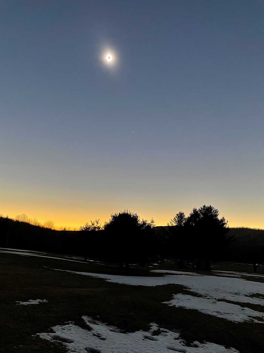 a landscape in low light with a bright orb at the top with a black circle in the middle of it