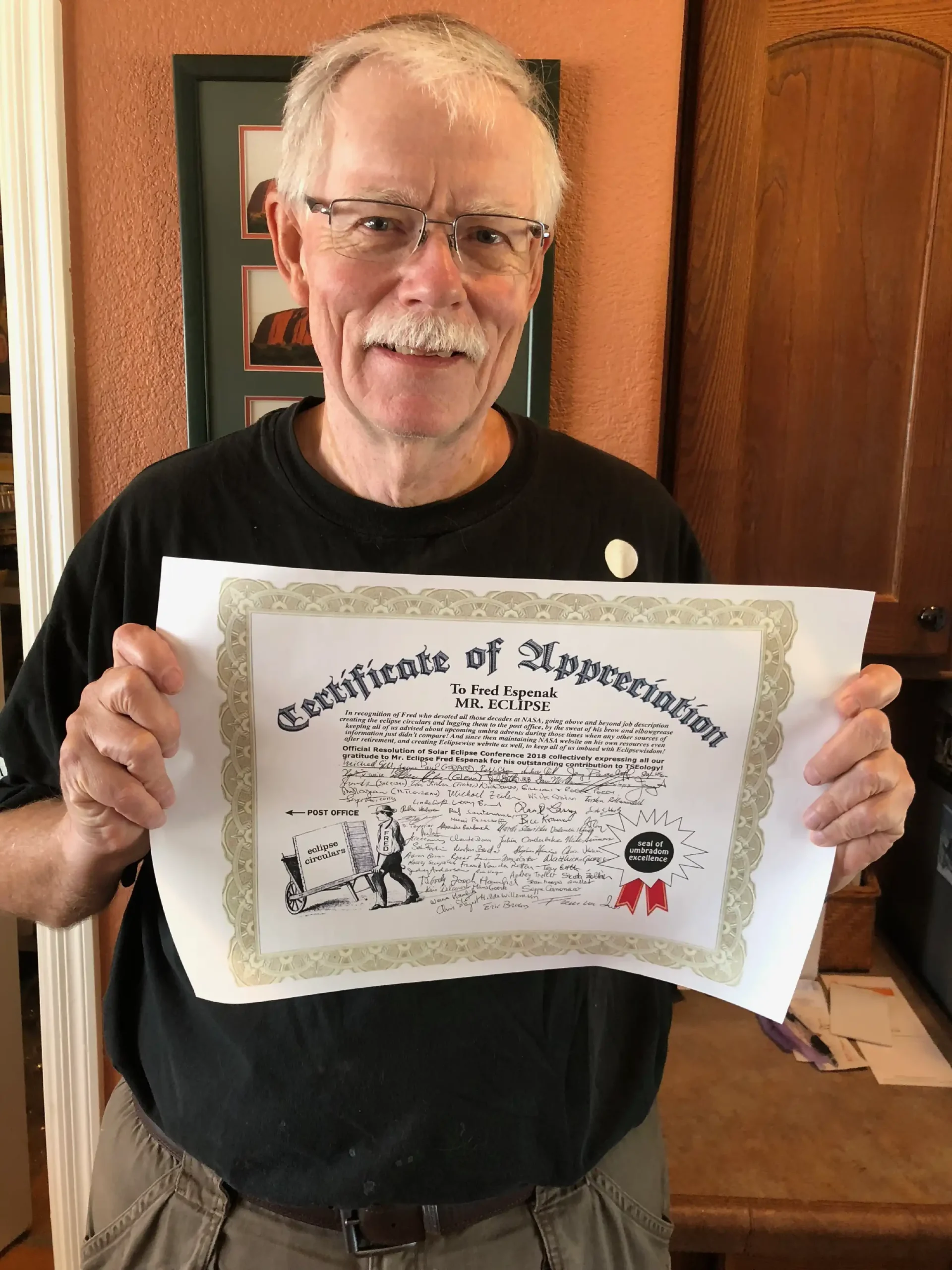 Man holding paper that says "Certificate of Appreciation, to Fred Espenak, Mr. Eclipse", with additional text and dozens of signatures